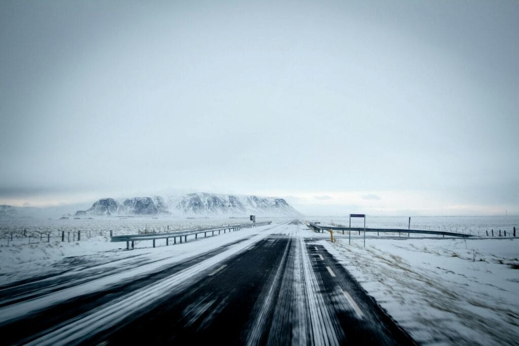 A serene winter scene with a snow-covered highway leading towards distant mountains under a gray sky.