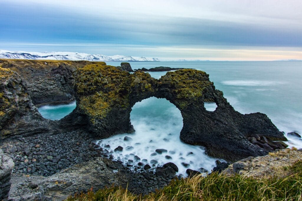 black and brown rock formation on sea under gray sky