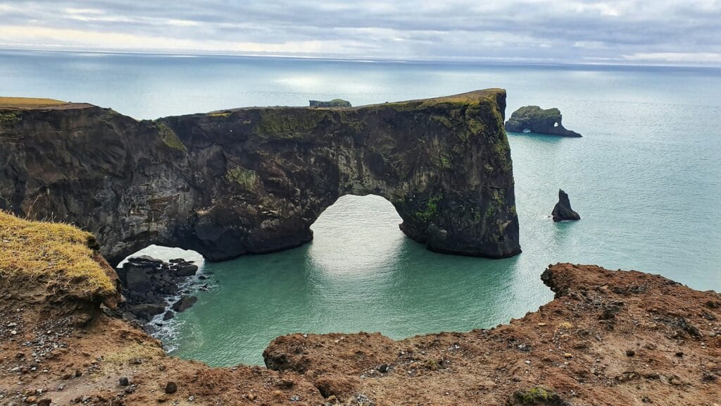 green and brown rock formation on sea under white clouds during daytime
