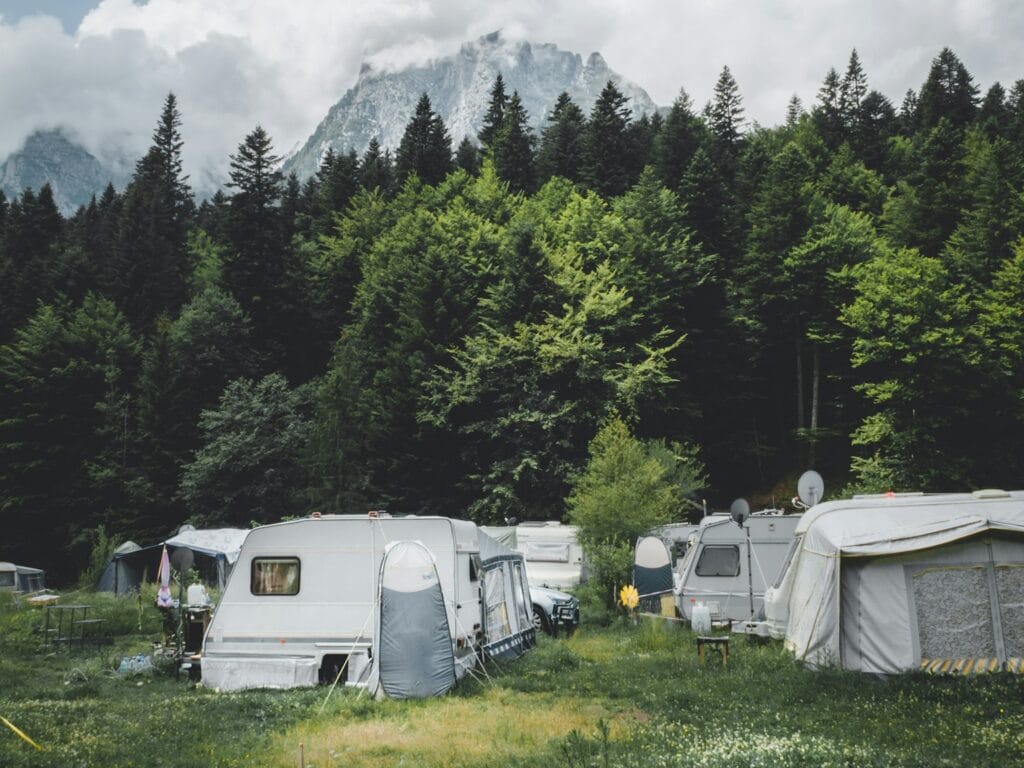 camper trailer near trees with snow-capped mountain at distance