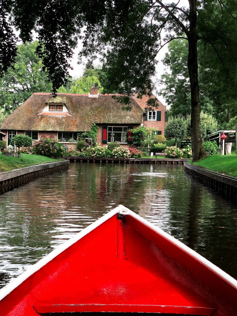 a red boat traveling down a river next to a house