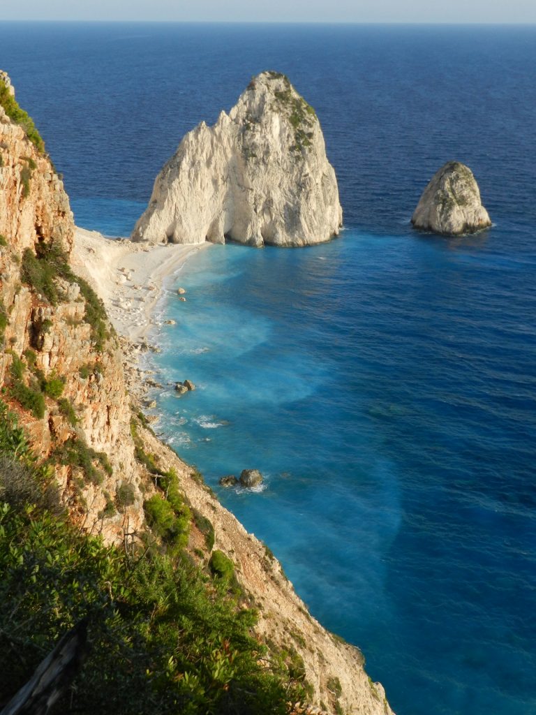 brown rocky mountain beside blue sea during daytime