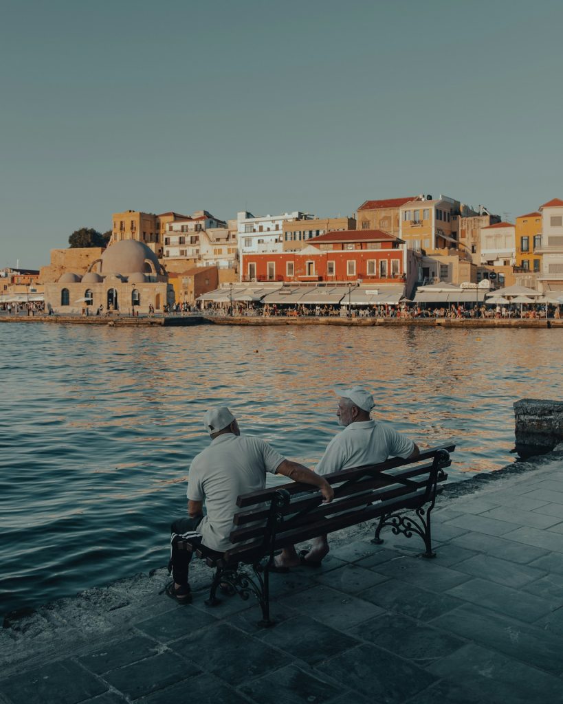 man in gray shirt sitting on bench near body of water during daytime
