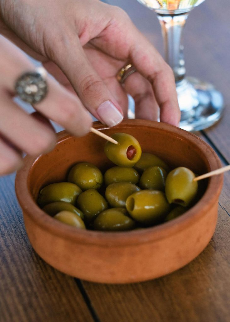 Close-up of hand picking green olives from a rustic bowl on a wooden table.